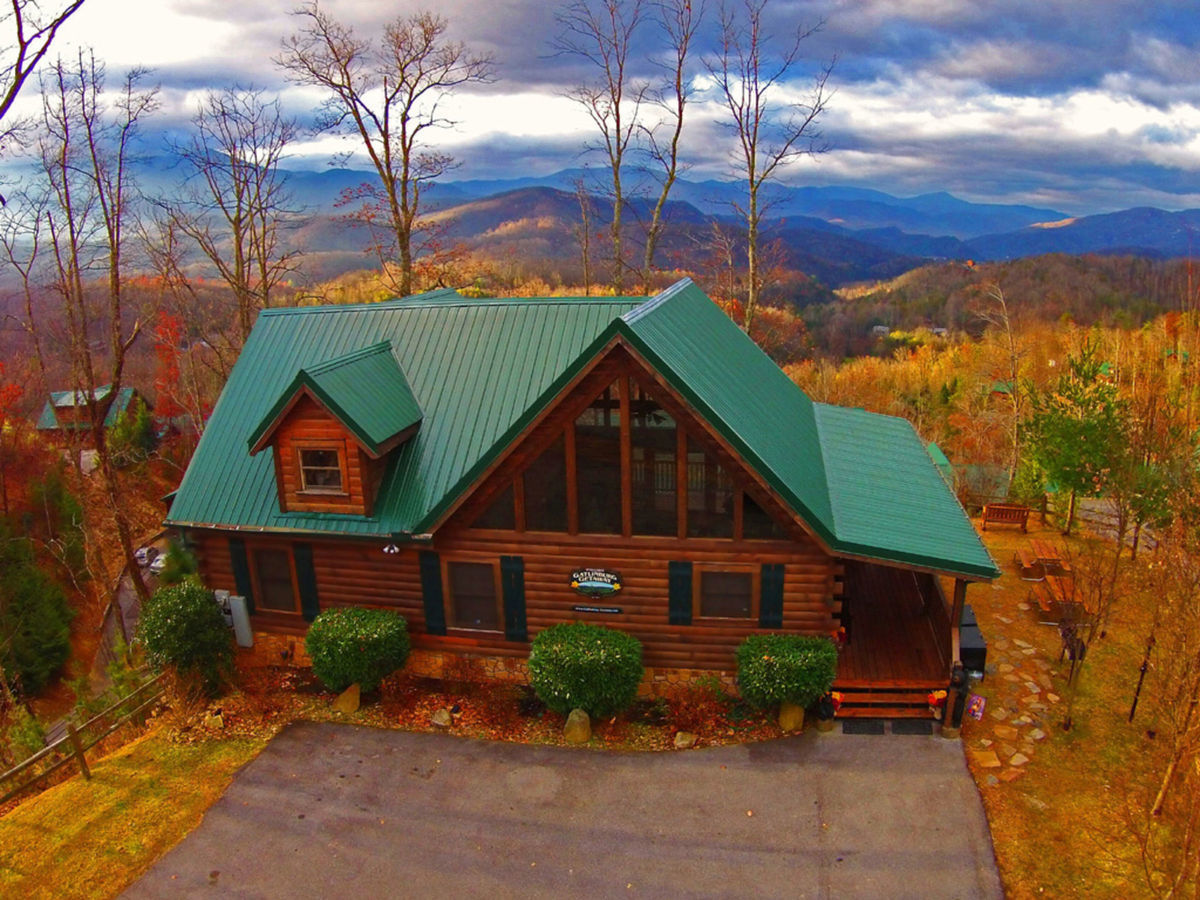 Mountains roll in the distance behind Gatlinburg Getaway, one of our best Smoky Mountain cabins. In the foreground, autumn has changed the leaves of the trees a bright, golden hue.